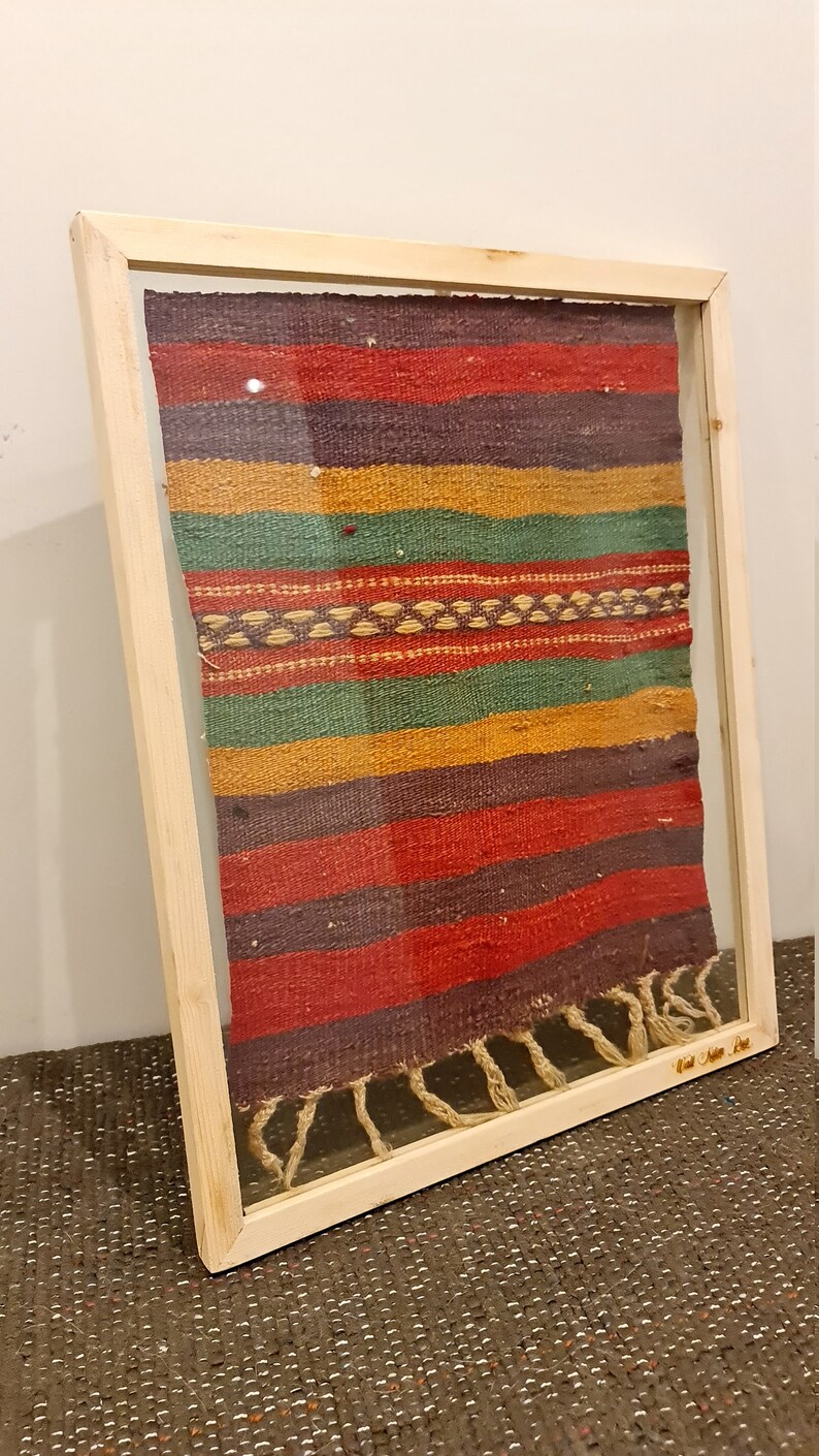 May include: A framed woven tapestry with colorful stripes in shades of red, green, yellow, and purple. The tapestry has a fringe border and is framed in a natural wood frame.