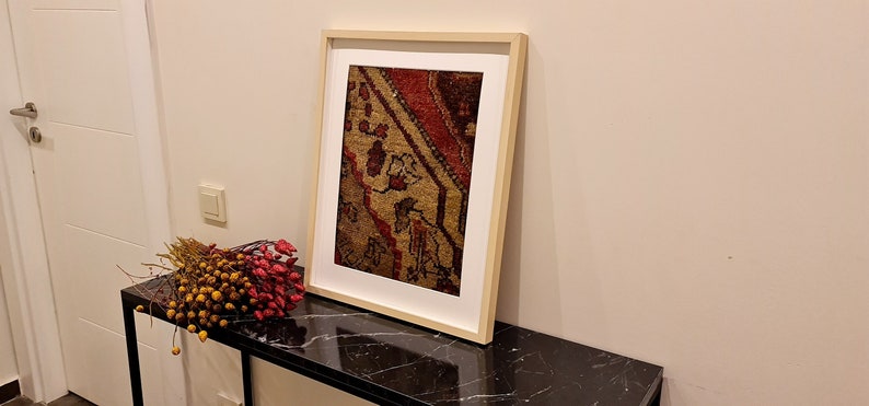 May include: A framed print of a vintage rug with a red, brown, and beige pattern. The frame is a light wood color and the print is on a white background.
