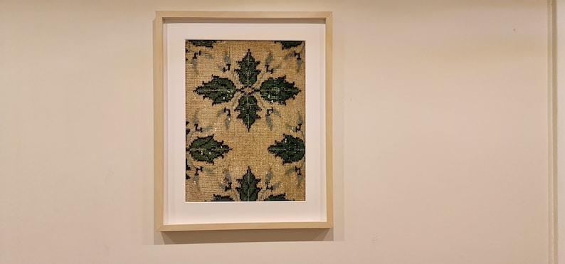 May include: A framed artwork featuring a beige background with a repeating pattern of green leaves.