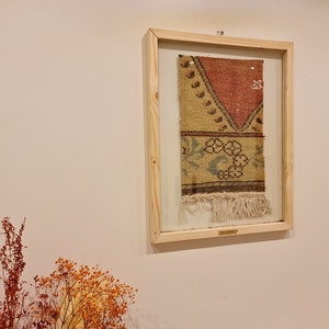 May include: A framed piece of vintage fabric with a colourful geometric pattern and fringe. The fabric is displayed in a light wood frame with a glass front.