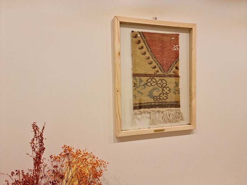 May include: A framed piece of vintage fabric with a colourful geometric pattern and fringe. The fabric is displayed in a light wood frame with a glass front.