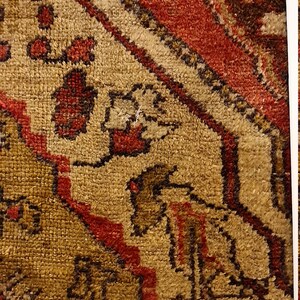 May include: Close-up of a red, brown, and beige patterned rug with intricate designs. The rug has a textured surface and is framed in a white frame.