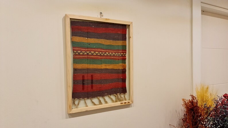 May include: A framed multi-colored woven tapestry with a fringe. The tapestry is made of different shades of red, orange, yellow, green, and brown.