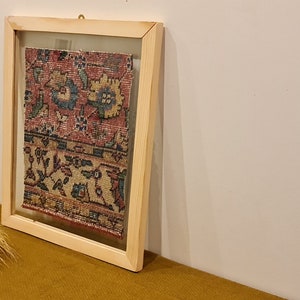Pu&ograve; includere: Un pezzo di tessuto incorniciato con un motivo floreale colorato in tonalit&agrave; di rosso, blu e giallo. Il tessuto &egrave; esposto in una cornice di legno chiaro con un fronte di vetro.