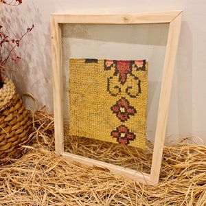 Puede incluir: Un trozo de tela amarilla enmarcado con un patr&oacute;n floral rojo y negro. La tela se muestra en un marco de madera con un frente de vidrio.