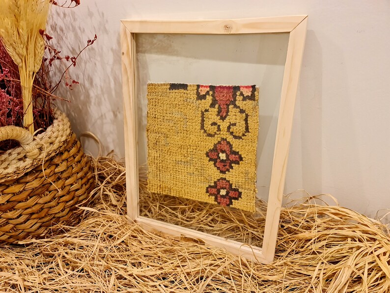 Puede incluir: Un trozo de tela amarilla enmarcado con un patr&oacute;n floral rojo y negro. La tela se muestra en un marco de madera con un frente de vidrio.
