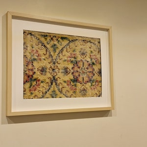May include: A framed print of a vintage rug with a floral pattern in shades of yellow, red, blue, and green.