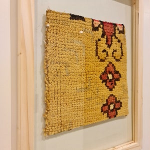 Puede incluir: Una alfombra kilim amarilla y roja enmarcada con un patr&oacute;n floral. El marco es de madera natural y tiene una etiqueta que dice "Alfombra kilim de pared".