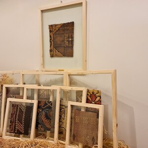 May include: A collection of framed fabric samples with various patterns and colours, displayed on a wall with a light brown background.