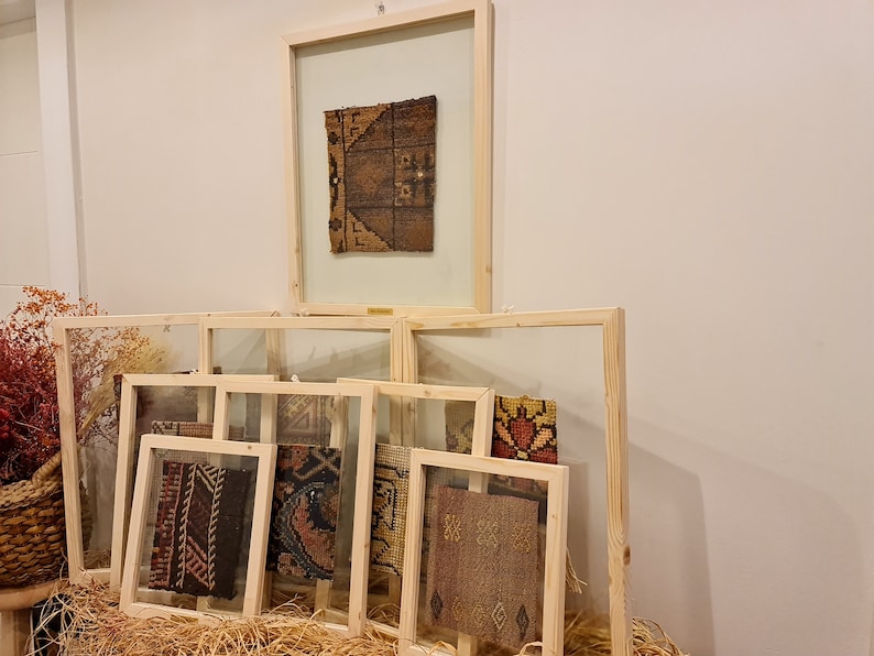 May include: A collection of framed fabric samples with various patterns and colours, displayed on a wall with a light brown background.