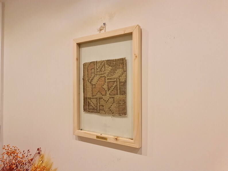 May include: A framed piece of woven fabric with a geometric pattern in shades of brown and beige. The frame is made of natural wood and has a glass front.