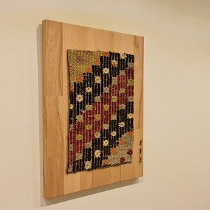 Puede incluir: Un tapiz tejido colorido con patrones geom&eacute;tricos en tonos rojos, negros, blancos y beige est&aacute; enmarcado en una tabla de madera.