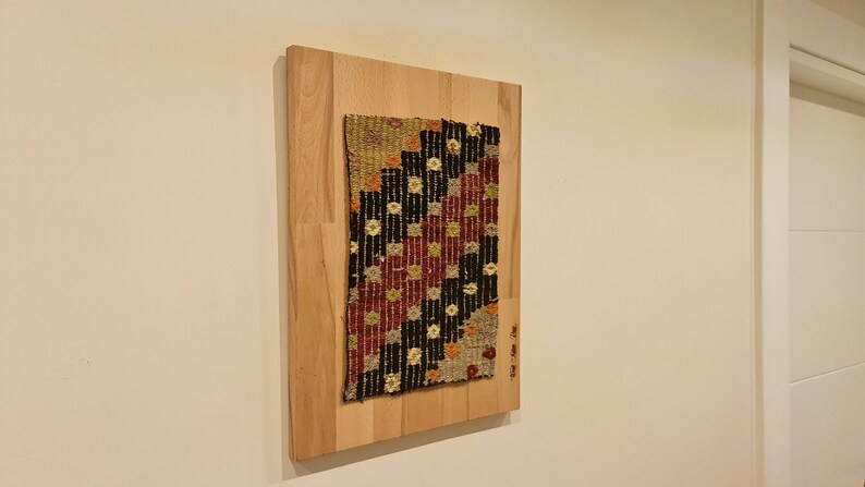 Puede incluir: Un tapiz tejido colorido con patrones geom&eacute;tricos en tonos rojos, negros, blancos y beige est&aacute; enmarcado en una tabla de madera.