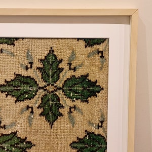 May include: A framed piece of art featuring a beige background with a repeating pattern of green leaves. The frame is a light wood colour with a white mount.