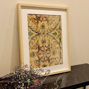 May include: A framed print of a vintage rug with a floral pattern in shades of yellow, red, and green. The rug is displayed on a black marble table.