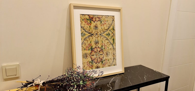 May include: A framed print of a vintage rug with a floral pattern in shades of yellow, red, and green. The rug is displayed on a black marble table.