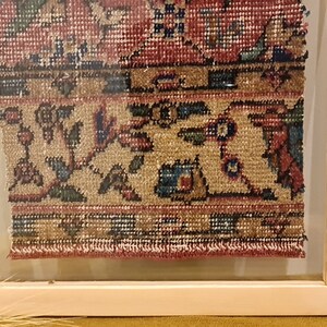 Pu&ograve; includere: Un pezzo di tappeto antico incorniciato con un motivo floreale in tonalit&agrave; di rosso, blu e beige. Il tappeto &egrave; incorniciato in una cornice di legno naturale.