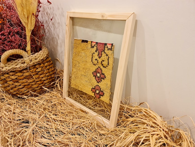 Puede incluir: Un trozo de tela estampada en amarillo y rojo enmarcado con un marco de madera. El marco est&aacute; sobre un lecho de paja.