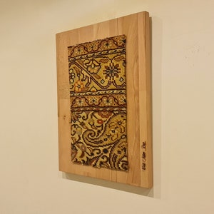 May include: A rectangular piece of wood with a colorful patterned fabric mounted on it. The wood is light brown and the fabric is a mix of yellow, orange, red, and black.