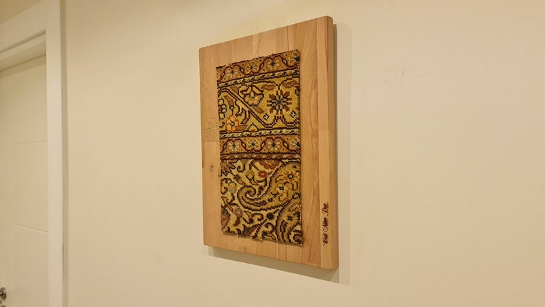 May include: A rectangular piece of wood with a colorful patterned fabric mounted on it. The wood is light brown and the fabric is a mix of yellow, orange, red, and black.