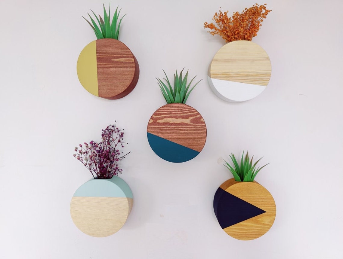 10 Fun Wall Hanging Planters To Bring Nature Indoor 9 May include: Five circular wooden wall planters with different colored paint designs. The planters are mounted on a white wall. The planters are filled with plants and flowers. The planters are a light wood color with a light blue, dark blue, white, yellow, and light green paint design.