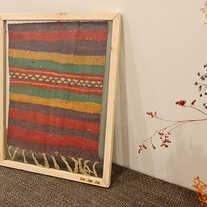 May include: A framed colorful woven rug with a wood frame. The rug has stripes of red, yellow, green, and blue.