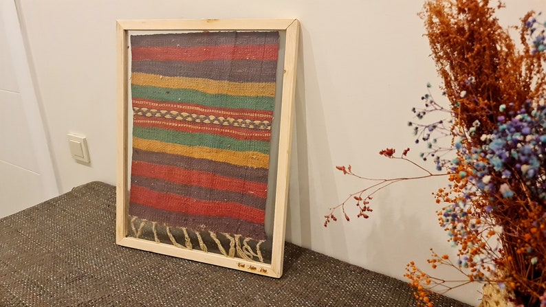 May include: A framed colorful woven rug with a wood frame. The rug has stripes of red, yellow, green, and blue.