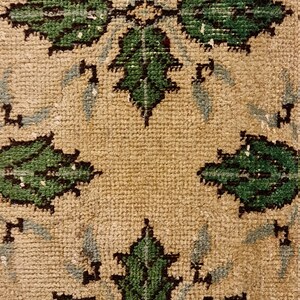 May include: A close-up of a beige rug with a repeating pattern of green leaves. The leaves are outlined in black and have a light blue background.
