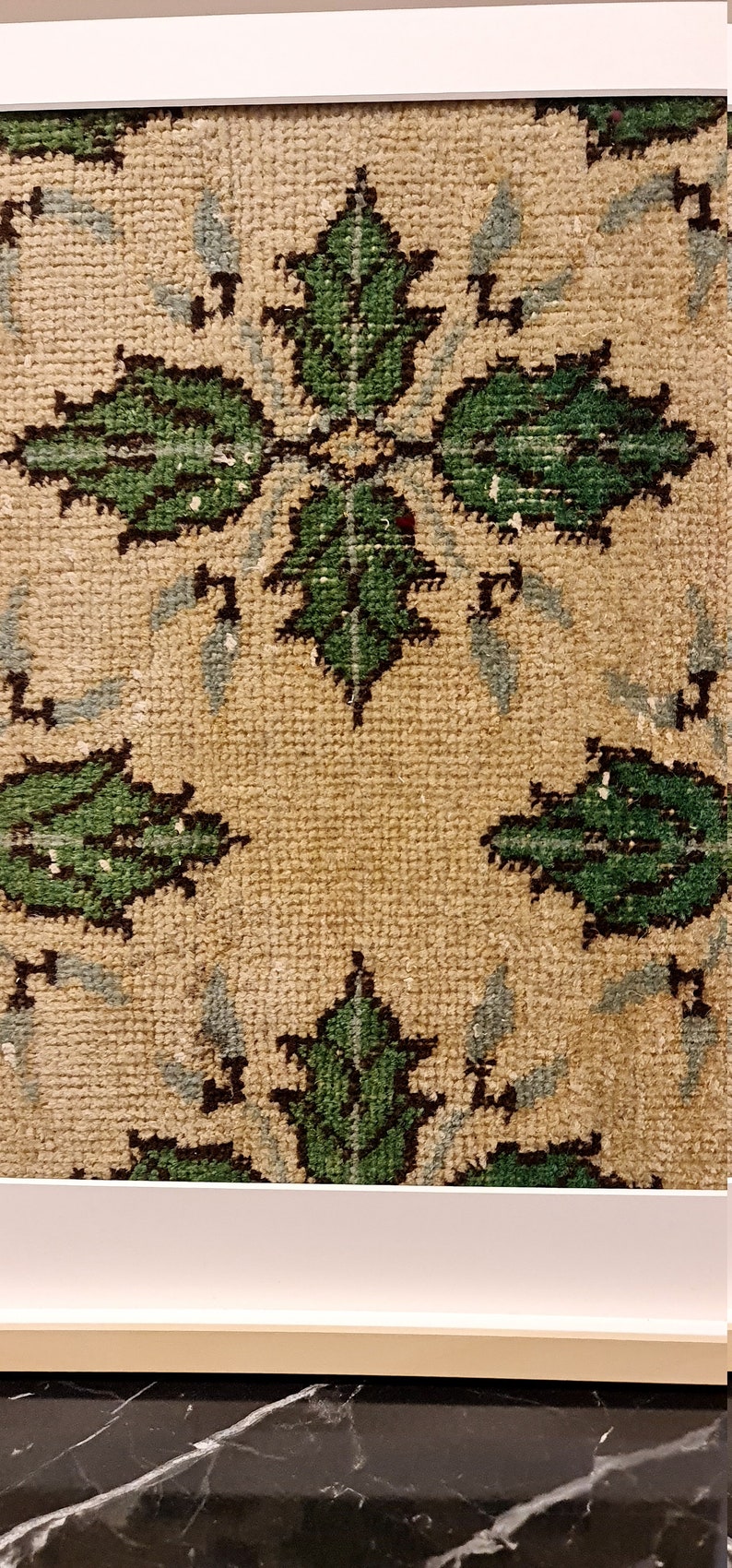 May include: A close-up of a beige rug with a repeating pattern of green leaves. The leaves are outlined in black and have a light blue background.