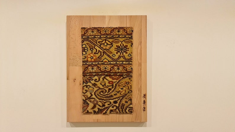 May include: A close-up of a framed piece of art featuring a colorful patterned rug on a wooden background. The text "From the Past" is visible in the lower right corner of the frame.