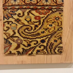 May include: A close-up of a colorful rug with intricate floral patterns, mounted on a wooden frame. The frame is labeled "Wall Art Rug".