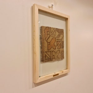 May include: A framed piece of woven fabric with a geometric pattern in shades of brown and beige. The frame is made of natural wood and has a glass front.