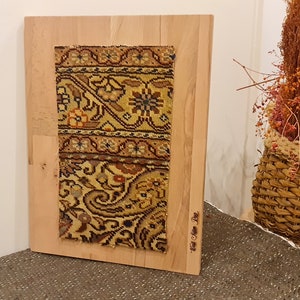 May include: A framed piece of fabric with a colorful floral pattern. The fabric is mounted on a wooden board and has the text "Hand Woven Pile" written on the bottom right corner.