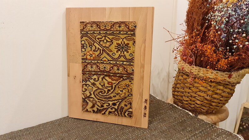 May include: A framed piece of fabric with a colorful floral pattern. The fabric is mounted on a wooden board and has the text "Hand Woven Pile" written on the bottom right corner.