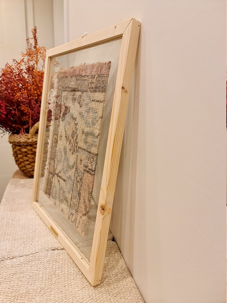 May include: A framed piece of fabric with a colorful pattern, displayed on a white wall. The frame is made of natural wood and has a glass front.