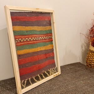 May include: A framed piece of colorful woven fabric with a wood frame. The fabric has stripes of red, purple, yellow, green, and brown.