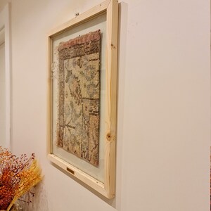 May include: A framed piece of antique fabric with a floral pattern in shades of pink, blue, and beige. The frame is made of natural wood and has a simple design.