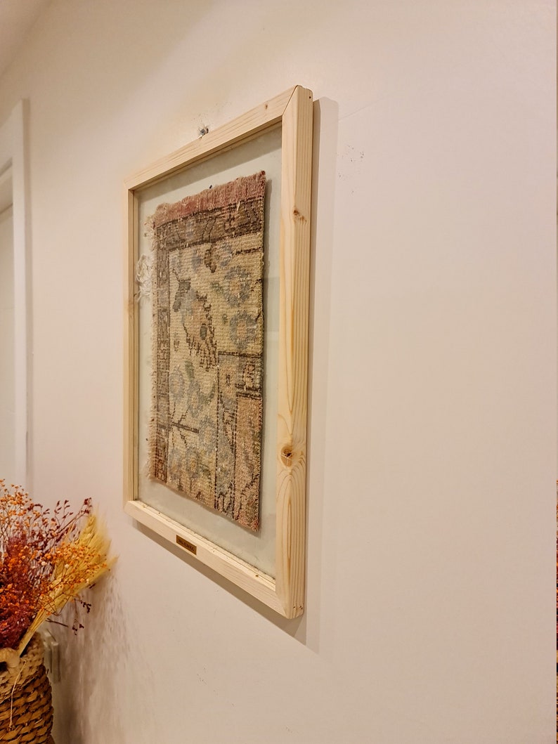May include: A framed piece of antique fabric with a floral pattern in shades of pink, blue, and beige. The frame is made of natural wood and has a simple design.