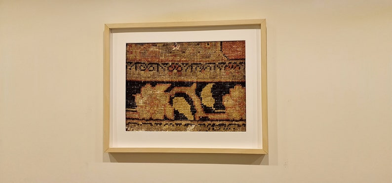 K&ouml;nnte beinhalten: Ein gerahmter Druck eines Ausschnitts einer Tapisserie mit einem geometrischen Muster in Braun-, Gelb- und Schwarzt&ouml;nen.