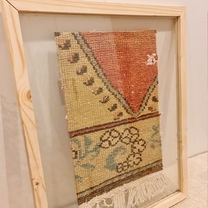 May include: A framed vintage rug with a cream, pink and brown geometric pattern. The rug has fringe on the bottom and is labelled "Wall Rug".