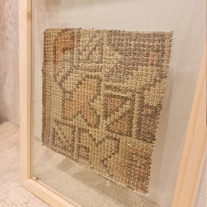 May include: A framed beige and brown woven wall kilim rug with a geometric pattern. The frame is made of natural wood and has a glass front. The label on the frame reads "Wall Kilim Rug".