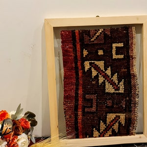 May include: A framed piece of antique fabric with a geometric pattern in shades of red, brown, and cream. The fabric is displayed in a natural wood frame with a glass front.