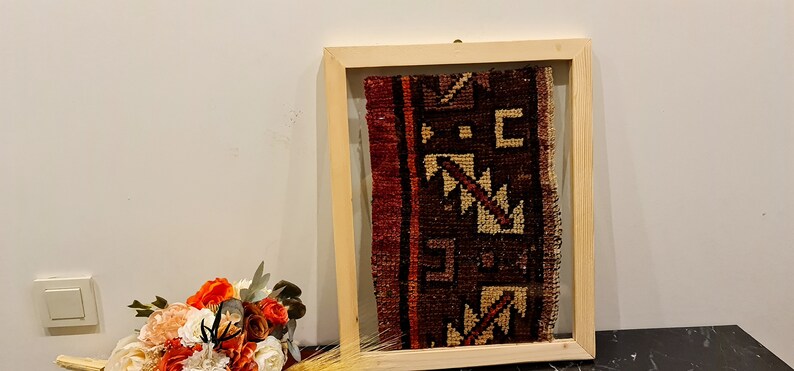 May include: A framed piece of antique fabric with a geometric pattern in shades of red, brown, and cream. The fabric is displayed in a natural wood frame with a glass front.