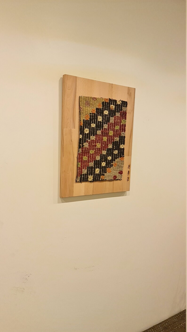 Puede incluir: Una pieza de tela tejida enmarcada con un patr&oacute;n geom&eacute;trico en tonos de rojo, negro, blanco y beige. La tela est&aacute; montada en un marco de madera claro.