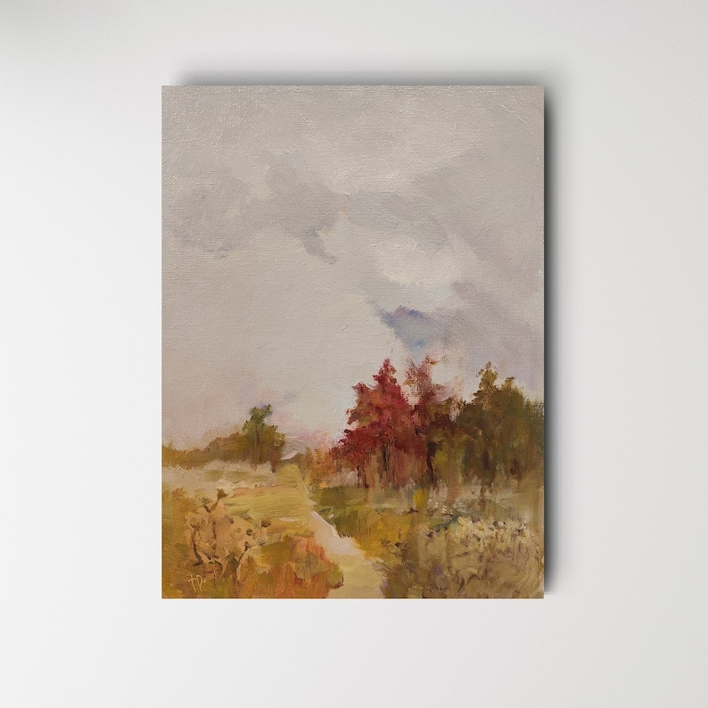 May include: An original oil painting of a landscape featuring a cloudy sky and a path leading to a cluster of trees. The trees display a mix of red, green, and brown hues, with a muted color palette overall. The artwork is mounted on a white surface.