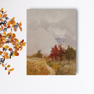 May include: An oil painting depicts a landscape with a path leading to a cluster of trees. The trees display red and green foliage under a cloudy sky. The painting has a muted color palette with shades of beige, brown, and gray.