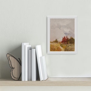 May include: A framed landscape painting with a white border depicts a field and trees under a cloudy sky. The painting is displayed on a shelf with white books and a wooden butterfly bookend.