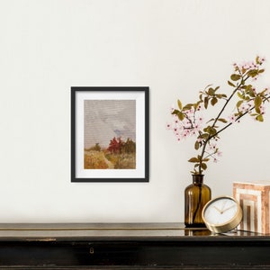 May include: A framed landscape art print featuring a path leading to red trees under a cloudy sky. The artwork is in a black frame, displayed on a black surface, with a vase of pink flowers and a gold clock nearby.