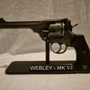 May include: A vintage Webley-Mk VI revolver, displayed on a black stand. The revolver is a dark metallic color with intricate details. The stand has the text "WEBLEY - MK VI" in white.