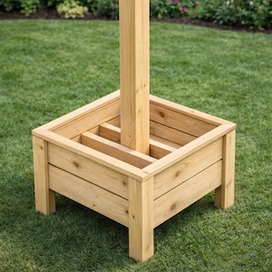 May include: A square wooden planter box with a central post, ideal for outdoor use. The planter is constructed from light-colored wood, featuring horizontal planks and a sturdy base. The post rises from the center, designed to support a structure like an umbrella or a flag.